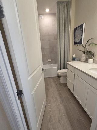 A bright bathroom with sleek white cabinetry, wood-look tile flooring, and a tiled tub/shower combo.
