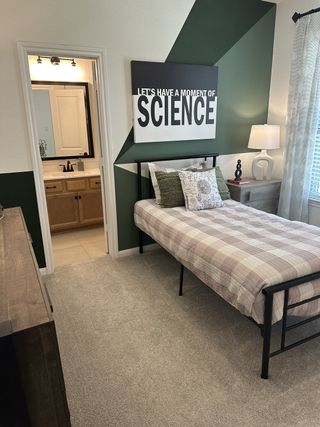 A modern bedroom with geometric wall art, cozy bedding, and an open view to the bathroom.