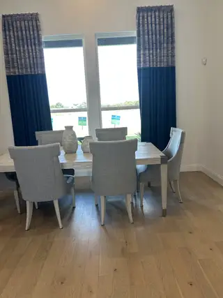 Model Home A modern dining area with elegant gray chairs, a light wood table, and large windows with stylish blue curtains.