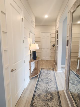 A bright and inviting hallway with elegant wall detailing, a large framed mirror, and a chic runner for a welcoming touch.
