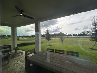 A cozy patio with a ceiling fan and outdoor seating offers serene views of a spacious green lawn and open sky.