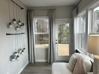 A cozy nook with a light sofa, hanging plants, and large windows. Neutral tones create a serene atmosphere.