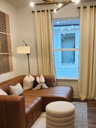 A cozy living room with a leather sectional, patterned pillows, and modern lighting, framed by elegant curtains.