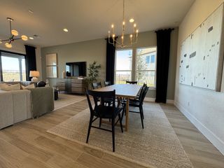 A modern dining area with a wooden table, chic black chairs, and contemporary lighting, opening to a cozy living space.
