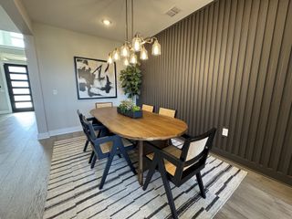 A modern dining room with a sleek wooden table, black chairs, striped rug, and an elegant light fixture.