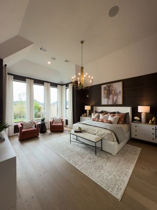A spacious bedroom featuring a plush bed, elegant chandelier, and cozy seating area with natural light pouring in.