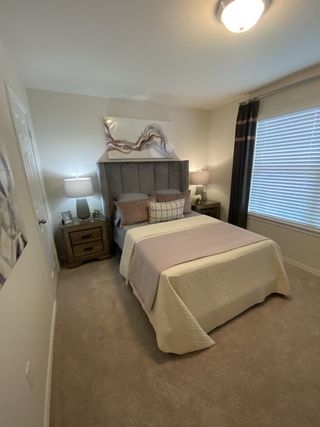 A cozy bedroom with a plush gray headboard, soft carpeting, and modern decor in soothing neutral tones.