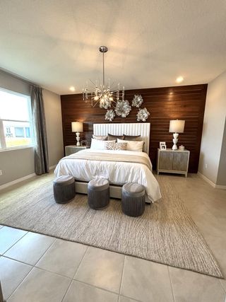A contemporary bedroom with a wood accent wall, stylish chandelier, and cozy seating.