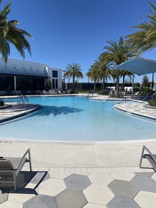 A stunning resort-style pool in the Del Webb eTown community by Del Webb (Jacksonville, FL) surrounded by swaying palm trees, shaded lounge areas, and a spacious sundeck for relaxation.