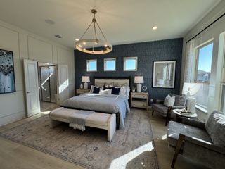 Model Home A luxurious bedroom featuring a chic chandelier, textured accent wall, and cozy seating by large windows.