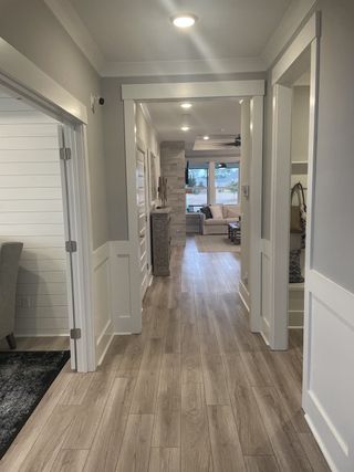 A welcoming hallway with wood flooring, light walls, and recessed lighting leading to a cozy living area with large windows.