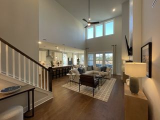 A spacious living area with high ceilings, modern furniture, and a kitchen view, featuring large windows and warm lighting.