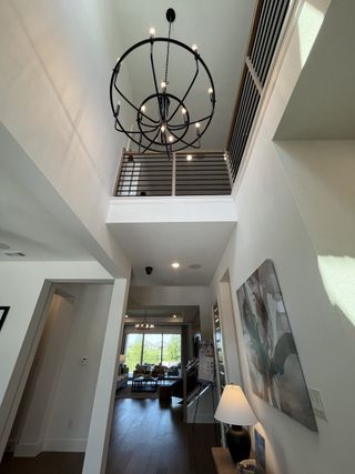 A modern foyer with a striking chandelier, high ceilings, and a view into a bright living area.