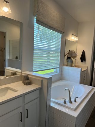 A cozy bathroom featuring a tiled bathtub, sleek vanity, and a large window with soft lighting.