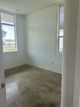 A bright room with textured white walls, tall windows, and a polished concrete floor.