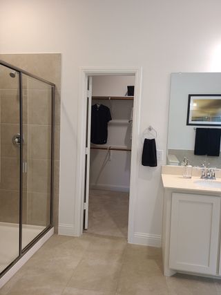 A modern bathroom with a tiled shower, sleek vanity, and walk-in closet access for seamless organization.