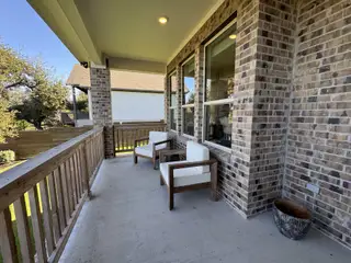 A cozy porch with brick walls, wooden railing, and modern seating, perfect for relaxation.