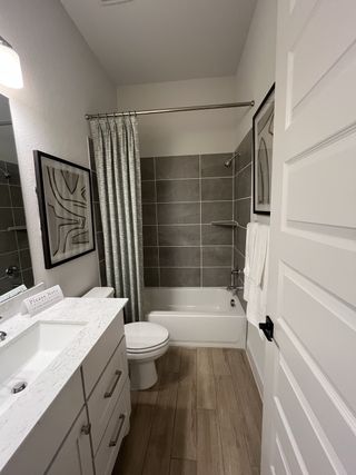 Model Home A modern bathroom featuring a sleek vanity, large tiles in the shower, and warm wood-style flooring.