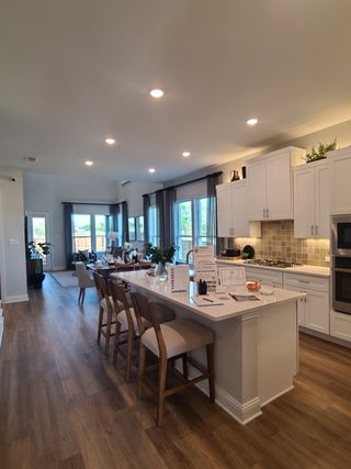 Model Home A modern kitchen with white cabinets, an island with bar stools, and wood flooring, offering ample natural light.