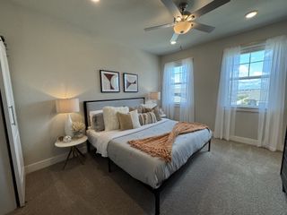 A cozy bedroom featuring modern décor, soft lighting, a plush bed, and large windows with sheer curtains for abundant natural light.