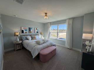 A cozy bedroom with soft gray walls, plush carpet, colorful abstract art, and a large window inviting natural light.