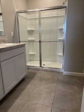 A modern bathroom with a sleek glass shower, granite countertop, and stylish gray tile flooring.