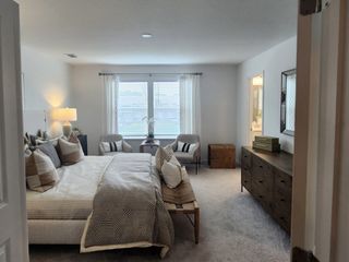 A spacious master bedroom with a cozy bed, soft carpeting, and large windows allowing natural light to fill the room.