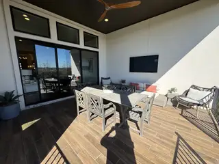 A cozy covered patio featuring an outdoor dining space, lounge seating, and elegant wood-look tile flooring.