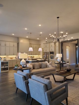 Open-concept living room with cozy seating, modern chandelier, and a spacious kitchen, all in neutral tones.