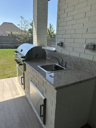 An outdoor kitchen with sleek brick design, granite countertops, and stainless steel appliances. Perfect for entertaining.