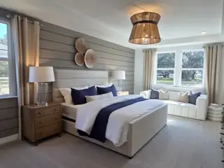 A serene bedroom with a plush bed, shiplap accent wall, and cozy seating by large windows, bathed in natural light.