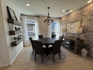 A cozy and stylish dining area with a rustic brick accent wall, a round wooden table with tufted chairs, and floating wooden shelves displaying decor.