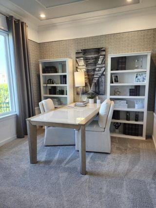 Model Home A chic home office with a sleek white desk, plush chairs, patterned wallpaper, and built-in shelves for a modern touch.