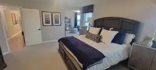 A cozy bedroom featuring a dark wood sleigh bed, plush white bedding with navy accents, and soft gray walls, leading to an adjoining space.