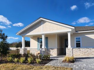 A charming beige home with stone accents and lush landscaping in Panther Creek by Brightland Homes (Jacksonville, FL).