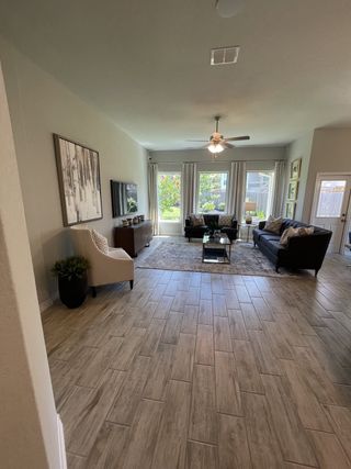 Model Home A spacious living room with tile flooring, a neutral color palette, dark sofas, and large windows bringing in ample natural light.