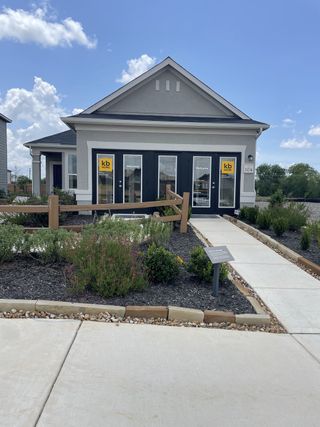 Street view A charming single-story model home in Mission del Lago by KB Home (San Antonio, TX), featuring a light gray exterior, a paved walkway, and a landscaped front yard.