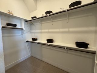 A spacious walk-in closet with white shelving, multiple rods, and neat black storage baskets.