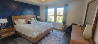 Model Home A cozy bedroom featuring a navy accent wall, wooden furniture, and large windows that illuminate the space.