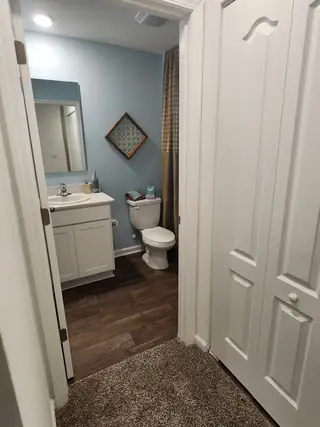 A cozy bathroom with a white vanity, hardwood floors, blue accent wall, and contemporary lighting.