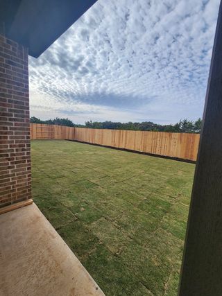 A spacious backyard with new sod and a wooden privacy fence under a blue sky with clouds.