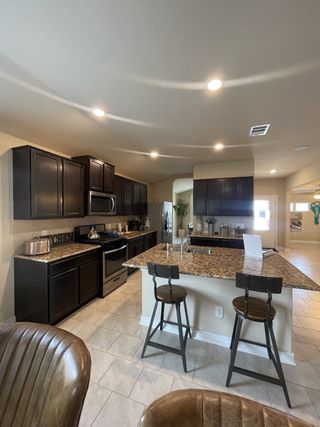 Model Home A spacious kitchen with dark wood cabinets, granite countertops, and a large island with seating flows into an open living area.