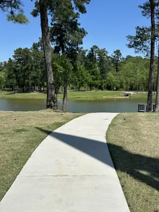 A scenic walkway by a tranquil pond amid lush greenery in Hills of Westlake by D.R. Horton (Conroe, TX).