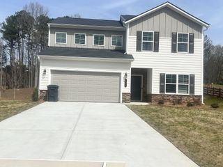 A charming two-story home in Swetlake Grove by Kerley Family Homes(Mableton, GA), features a white and gray exterior with dark shutters, a two-car garage, and a freshly poured concrete driveway.