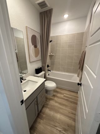 Model Home A stylish bathroom with a tiled shower, modern fixtures, and wood-look flooring in Vista Ridge by HistoryMaker Homes (Live Oak, TX).