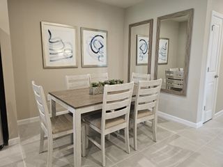 Model Home A cozy dining area featuring a wooden table, six chairs, abstract art, and mirrors for a stylish touch.