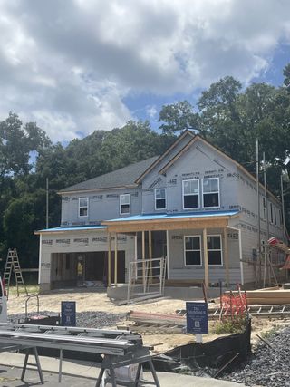 Street view Under-construction home with plywood siding and wraparound porch in Limehouse Farms: Townhomes by Lennar (Summerville, SC).
