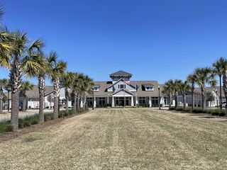 A grand community clubhouse with a central entrance, flanked by palm trees and a manicured lawn, in Four Seasons at Lakes of Cane Bay, Summerville, SC.
