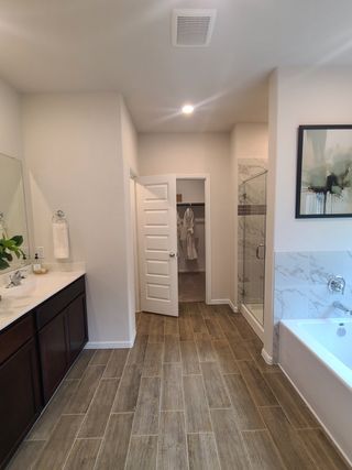 Model Home A modern bathroom with wood-look tile, dark vanity, glass shower, and relaxing bathtub.