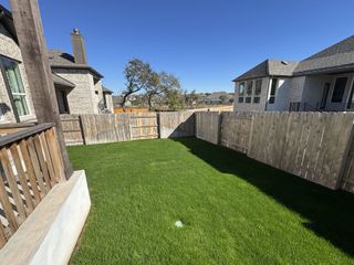 A charming backyard with lush green grass and a wooden fence in The Cottages at La Cima by Ashton Woods (San Marcos, TX).